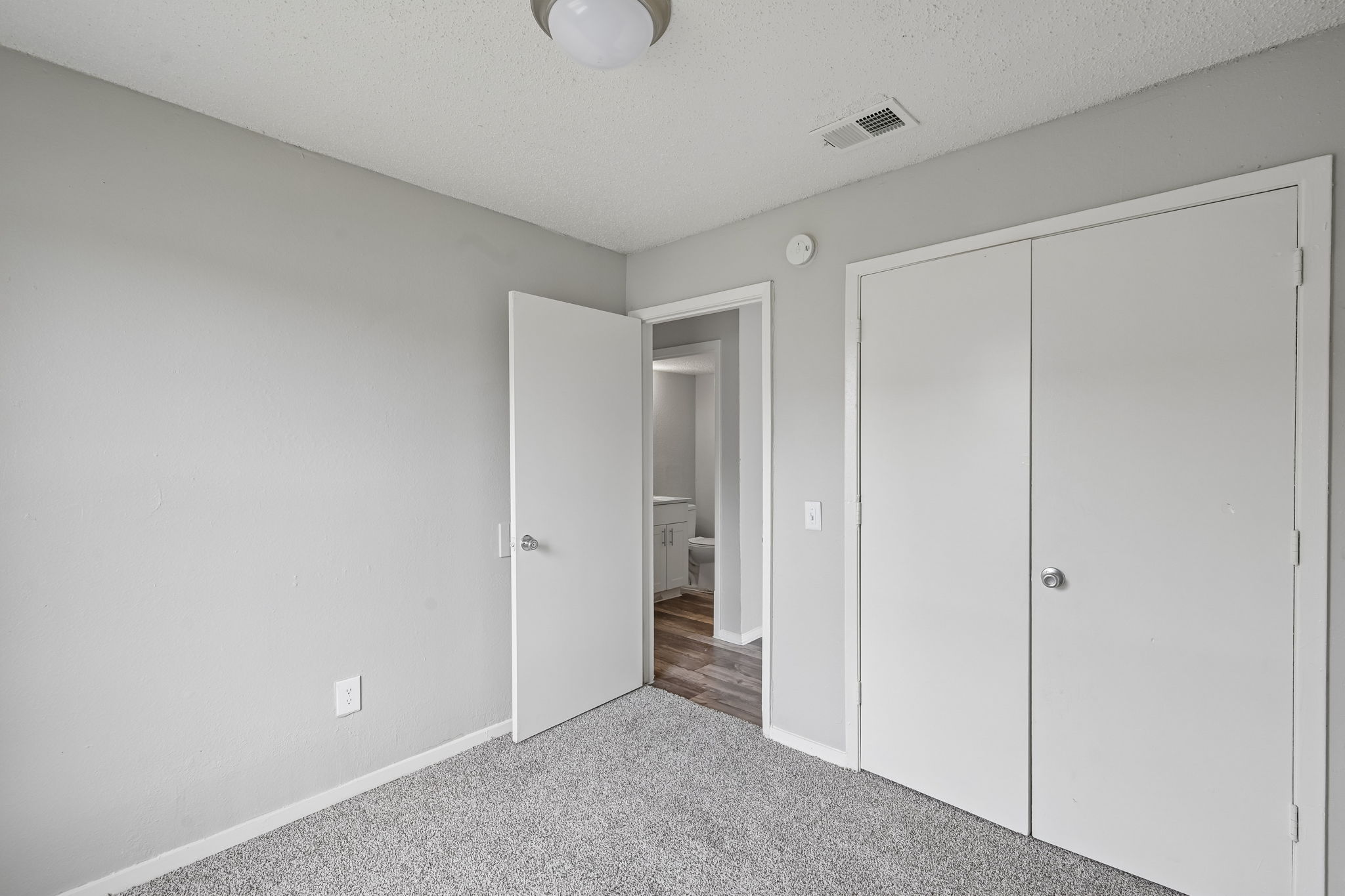 A white room with a carpeted floor and a doorway leading to another room.